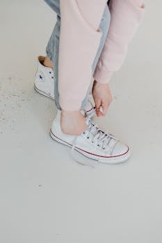Young adult tying white high-top sneakers on a minimalist background.