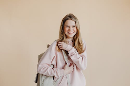 Free A Smiling Woman in Pink Sweater Carrying Her Backpack Stock Photo