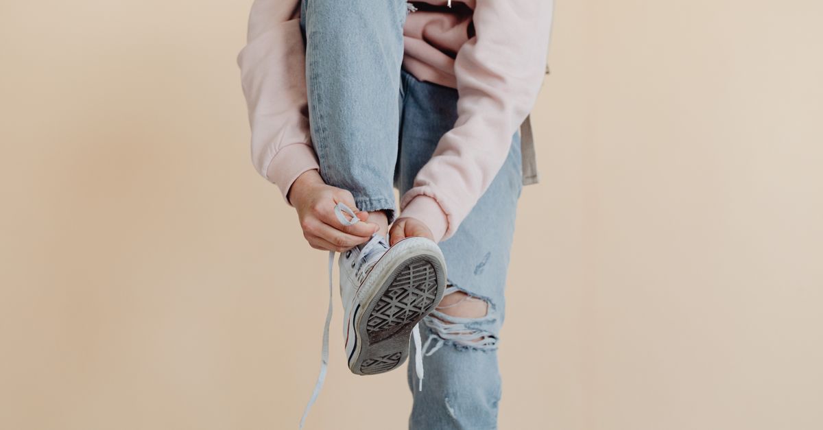 Close-up of a teenager tying shoelaces while wearing casual ripped jeans and a pink hoodie.