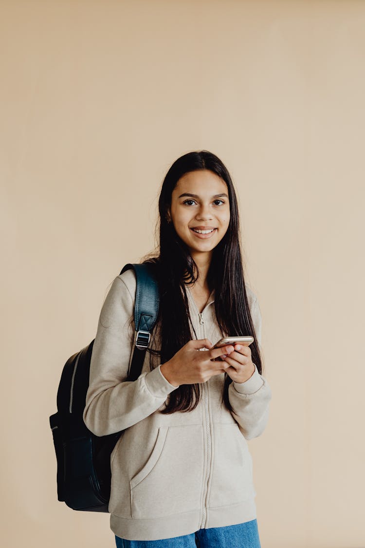 Female Teenager With Backpack Holding Her Phone