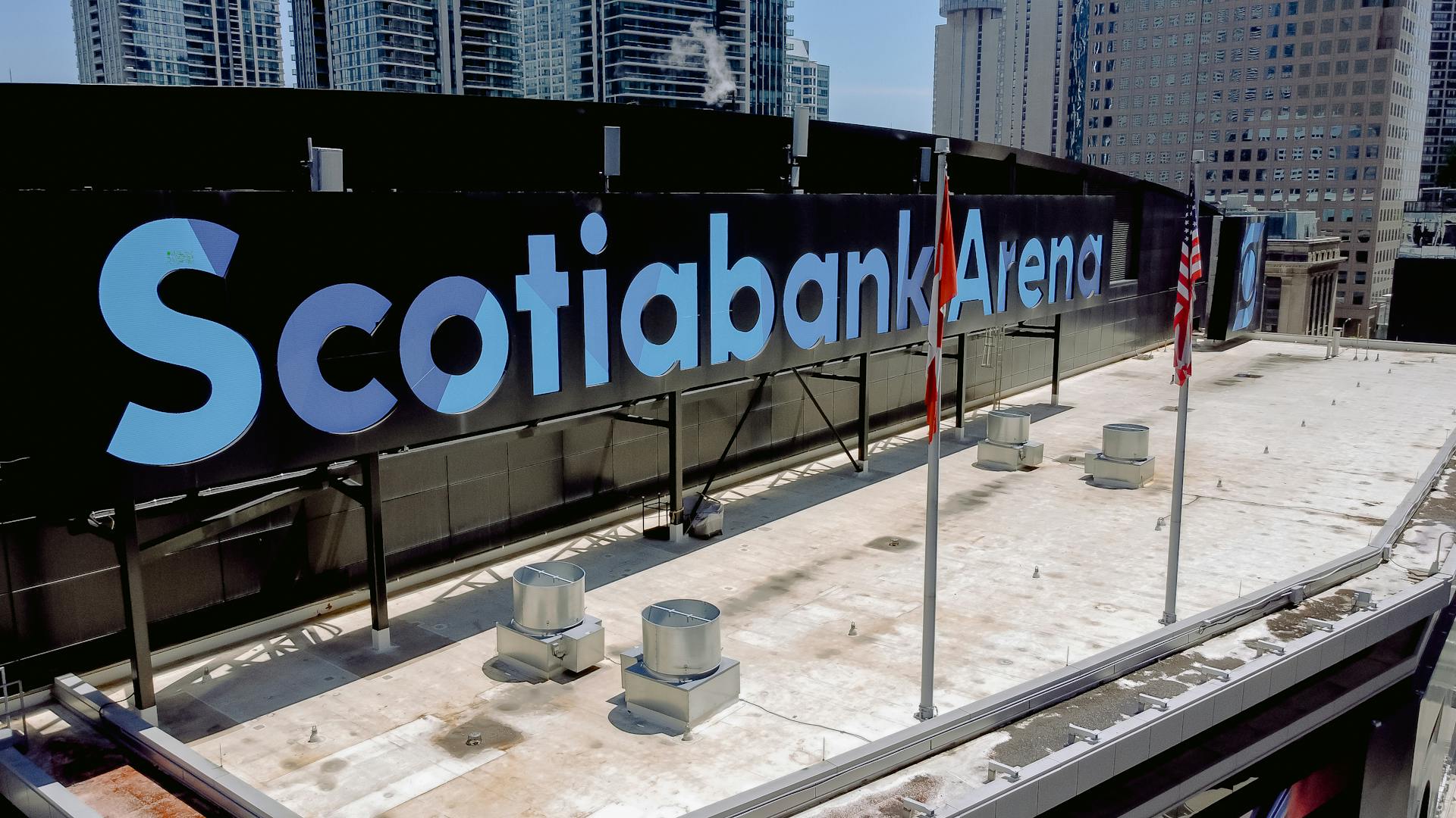 Aerial view of Scotiabank Arena's rooftop with flagpoles and city skyline background on a clear day.