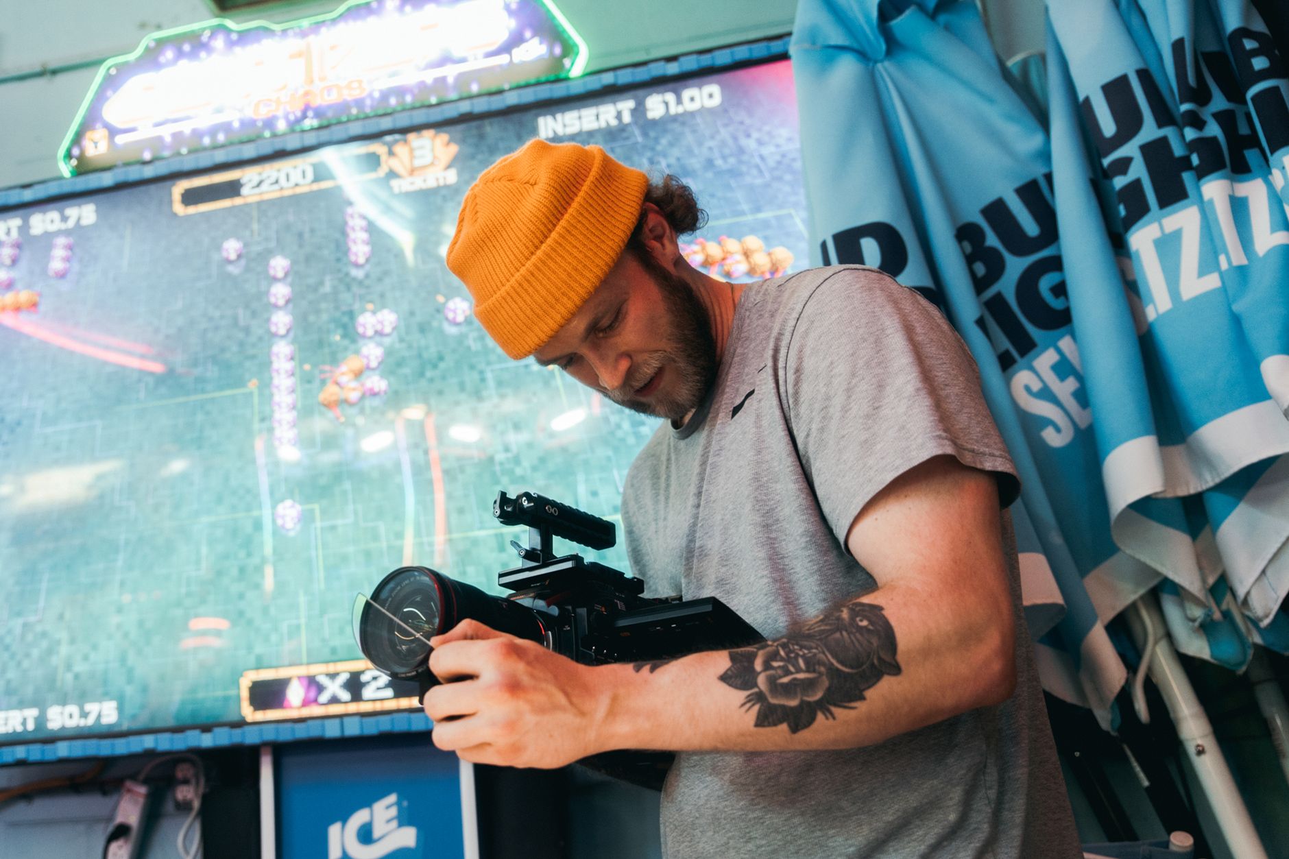 Man with tattoo filming in an arcade, using professional camera equipment.