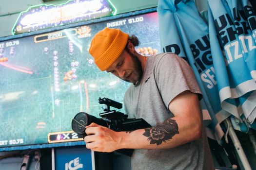 Man with tattoo filming in an arcade, using professional camera equipment.