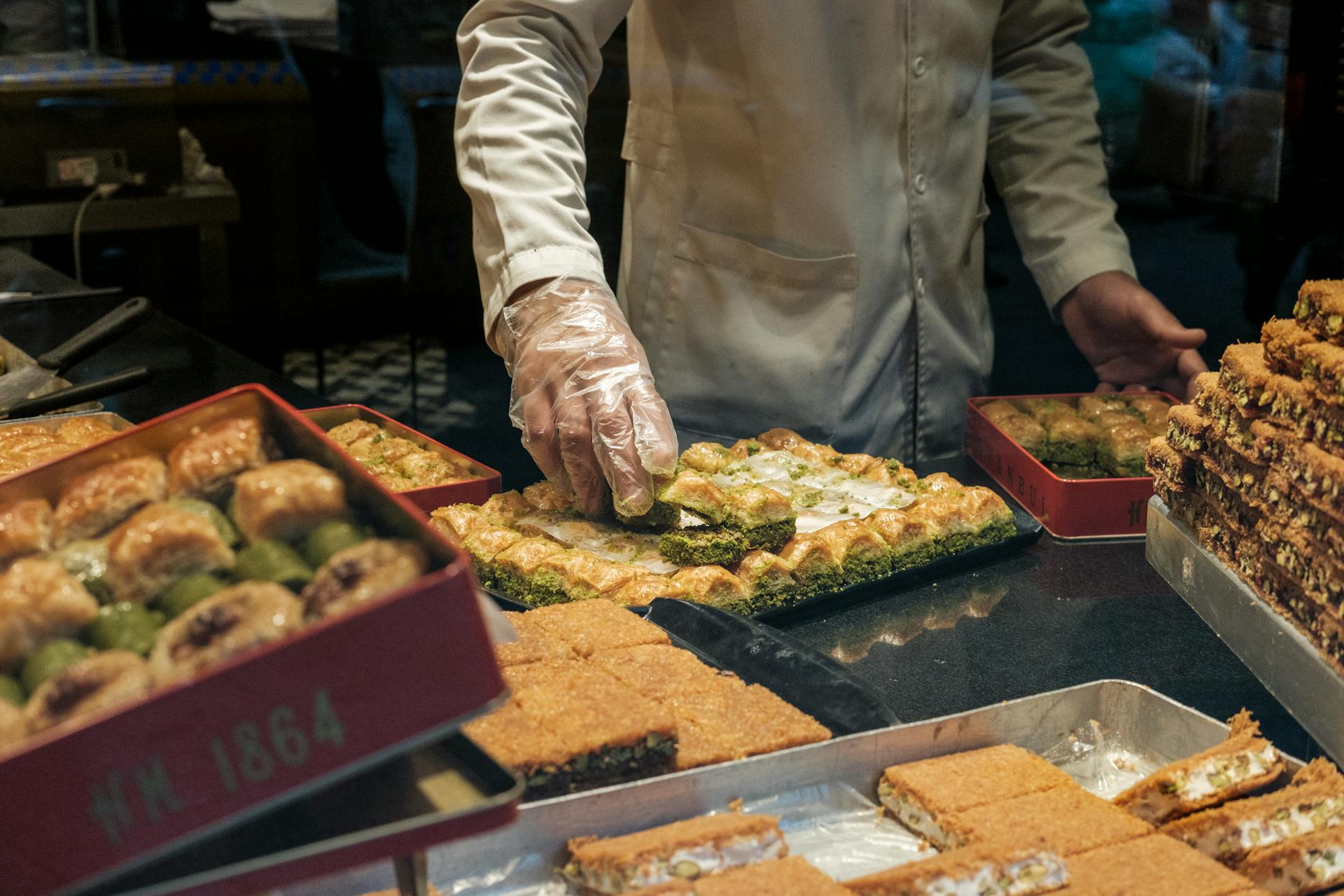 From above of anonymous crop male in gloves and white robe putting delicious fresh sweet dessert in container in local bakery shop