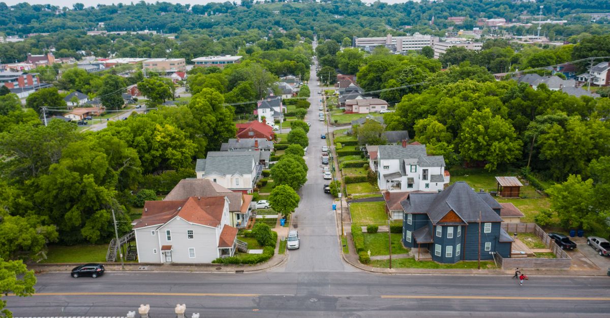 Aerial shot of a green suburban neighborhood with tree-lined streets and residential houses.