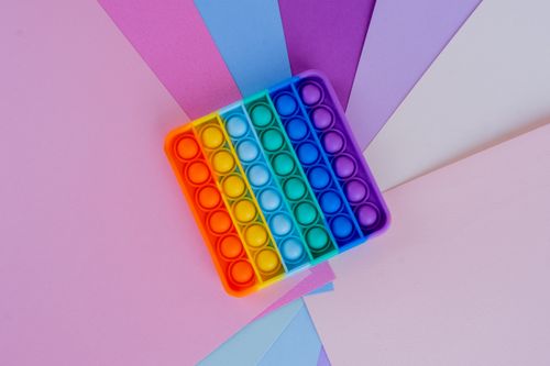 Free Rainbow pop it toy displayed on vibrant colored papers creating a playful scene. Stock Photo