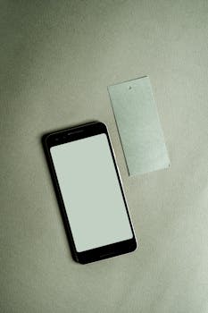 A smartphone with a blank screen alongside a tag on a green fabric surface. Perfect for mockup designs.