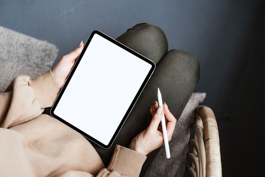 A person using a tablet with a stylus in a cozy, relaxed indoor setting on a chair.
