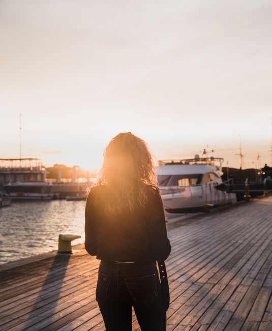 Back view of a woman with curly hair standing on Sopot pier at sunset, overlooking yachts.