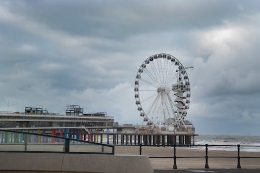 A dramatic shot of a coastal Ferris wheel amidst a cloudy sky by the sea.