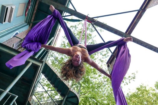 A skilled aerial acrobat performing an impressive pose using vibrant purple silk outdoors.