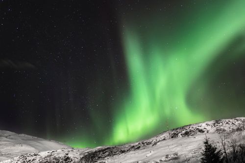 Free Stunning aurora borealis lights up the night sky above a snowy Norwegian hillside, showcasing nature's beauty. Stock Photo