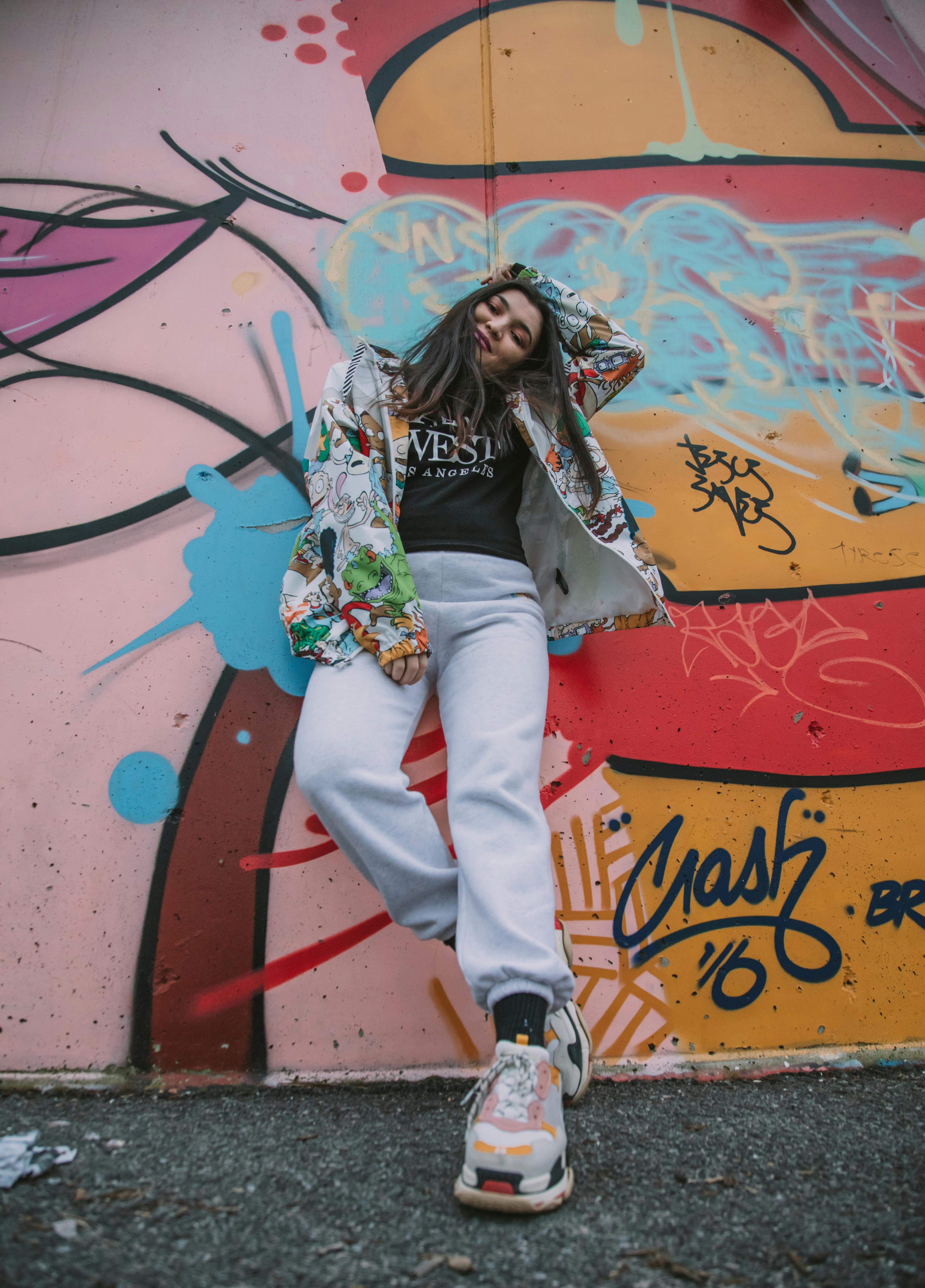 Young woman in trendy outfit posing against a colorful graffiti wall.