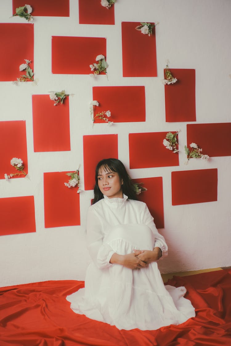 Woman In White Dress Sitting By The Wall On Red Sheets 