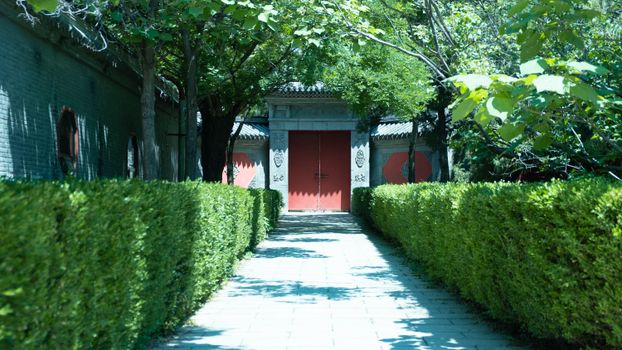 Peaceful garden path lined with hedges leading to a traditional red gate.