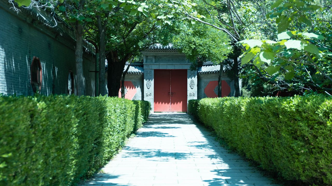 peaceful garden path lined with hedges leading to a traditional red ga