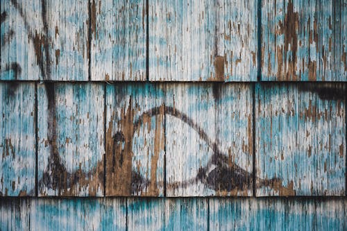 Abstract background of weathered old wooden wall of house with peeling paint and graffiti in daytime