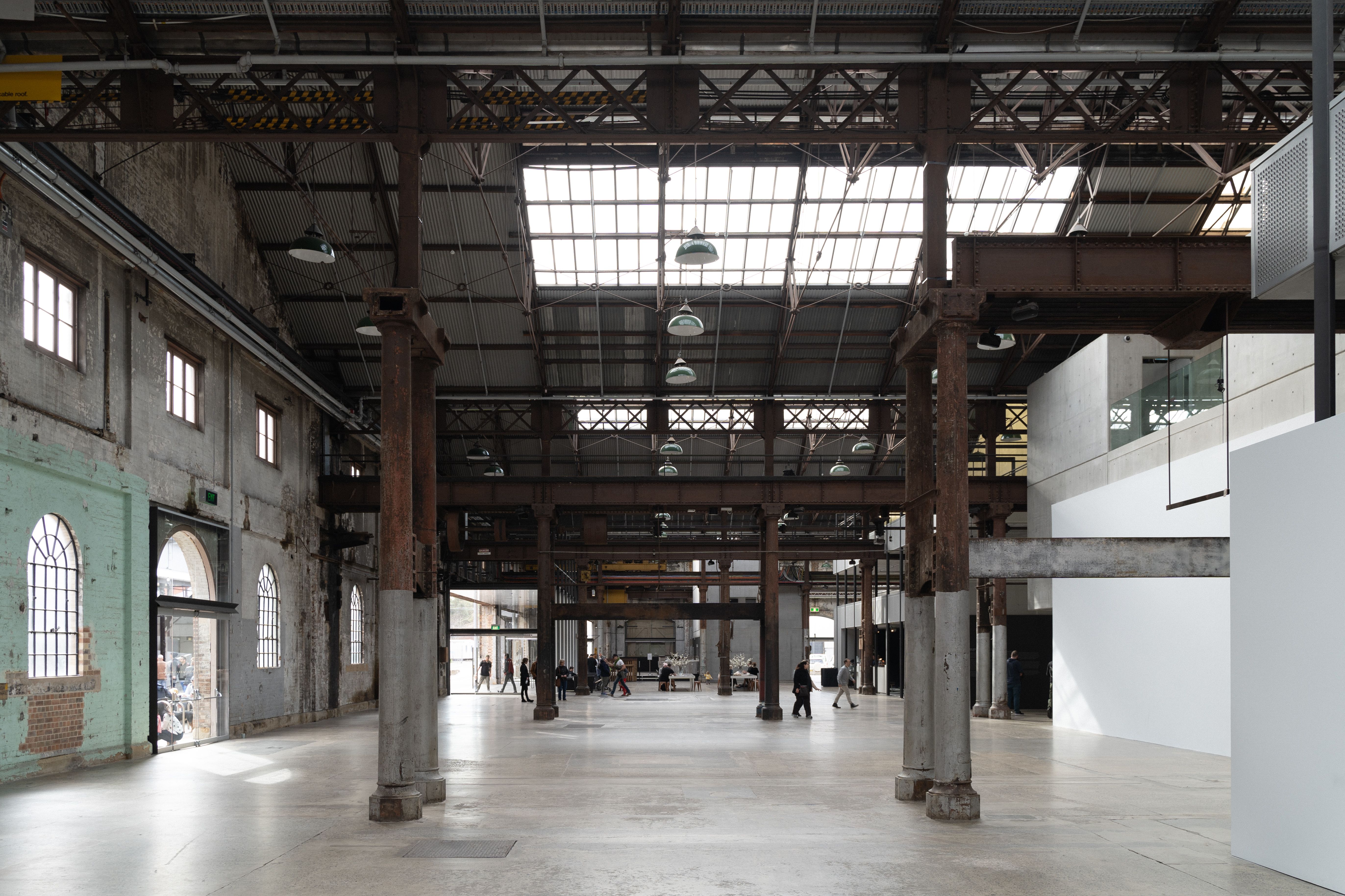A spacious, light-filled industrial warehouse in Sydney with exposed beams and people walking.