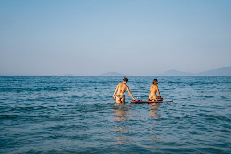 Woman In Bikini Sitting On Paddle Board In The Ocean