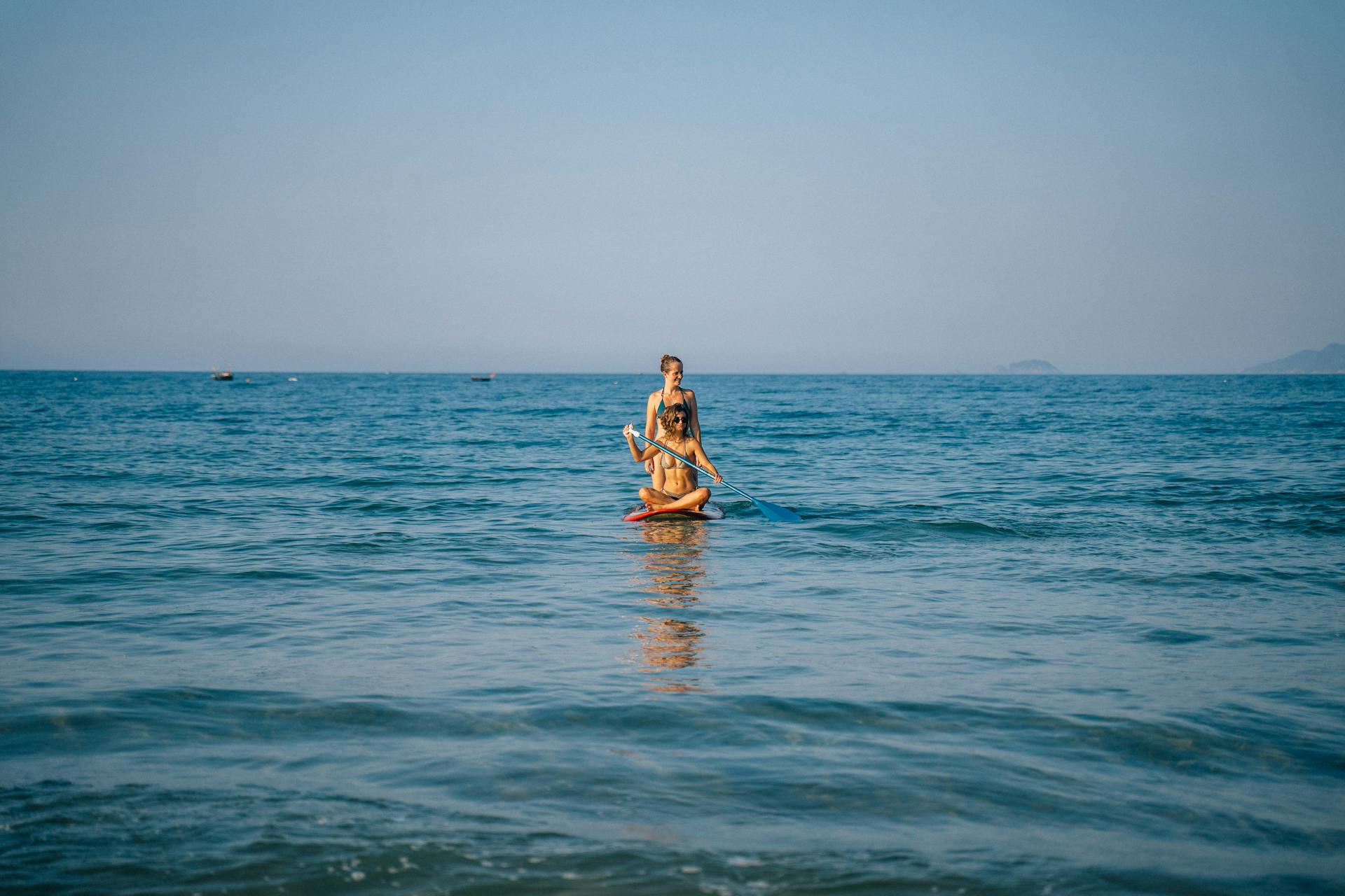 Two women enjoying paddle boarding on a calm ocean under a clear blue sky in Vietnam.