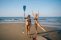 两名穿着比基尼的女子在越南拿着桨和冲浪板享受阳光明媚的海滩一天