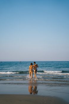 Two women in swimsuits embracing while standing on a Vietnam beach, with a clear blue sky and ocean waves.