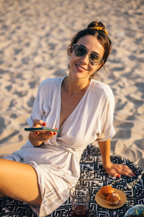 Free Smiling woman with sunglasses enjoying a sunny day on the beach in Vietnam, using a smartphone. Stock Photo