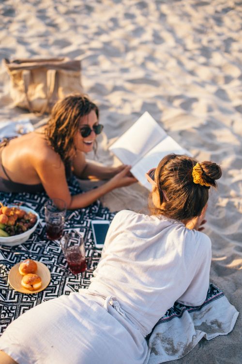 Free Two women relaxing with a picnic on a sunny beach in Vietnam, capturing a moment of friendship and leisure. Stock Photo