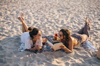 两名女子在越南的海滩上放松身心，阅读并享用零食