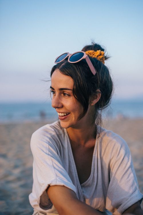Free Candid portrait of a woman enjoying a beach sunset in Vietnam, wearing sunglasses and smiling joyfully. Stock Photo