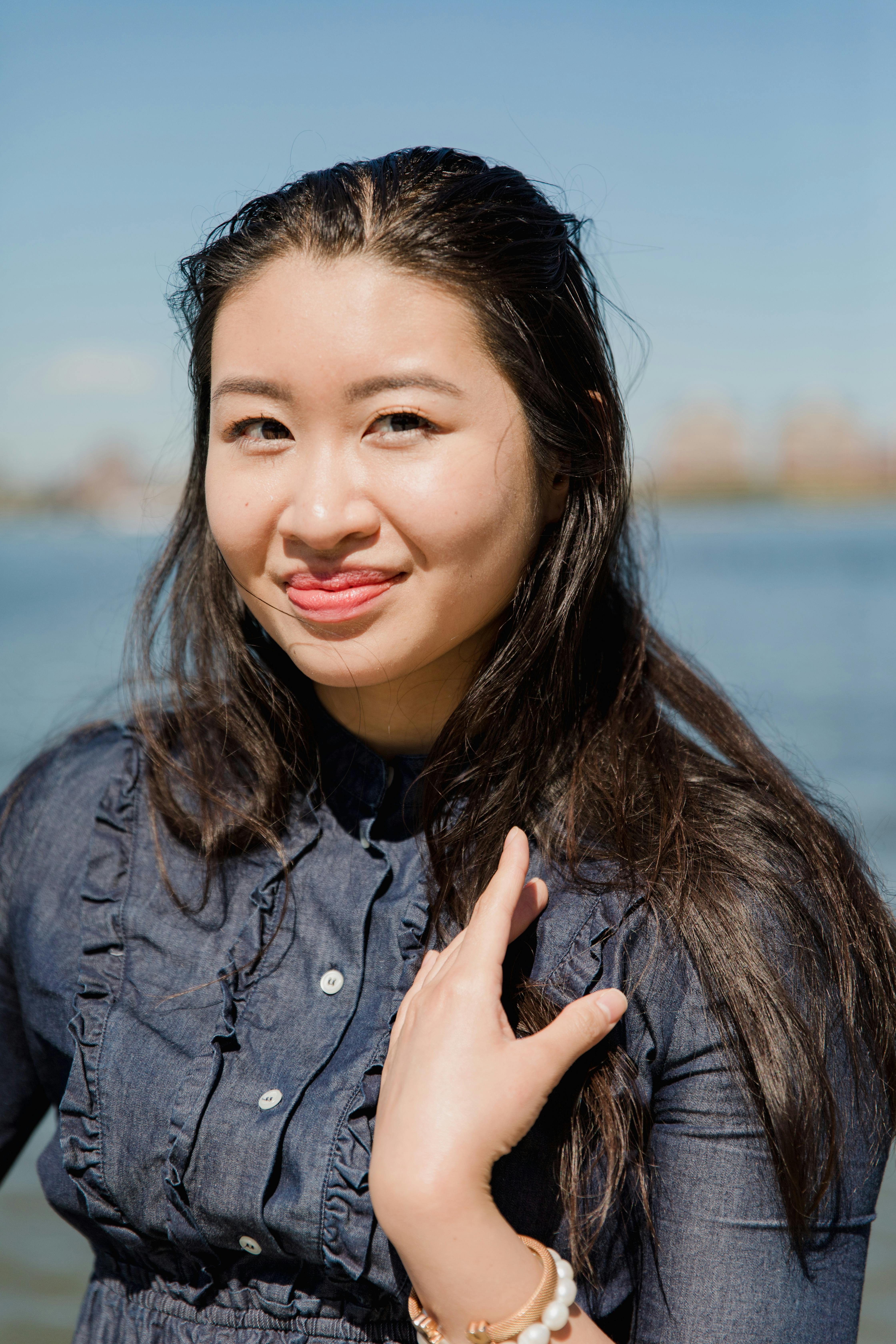 Asian woman with long hair smiling by the water on a sunny day.