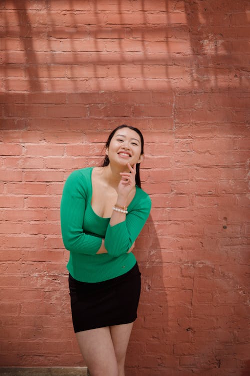 Woman in Green Shirt Standing beside Brown Brick Wall