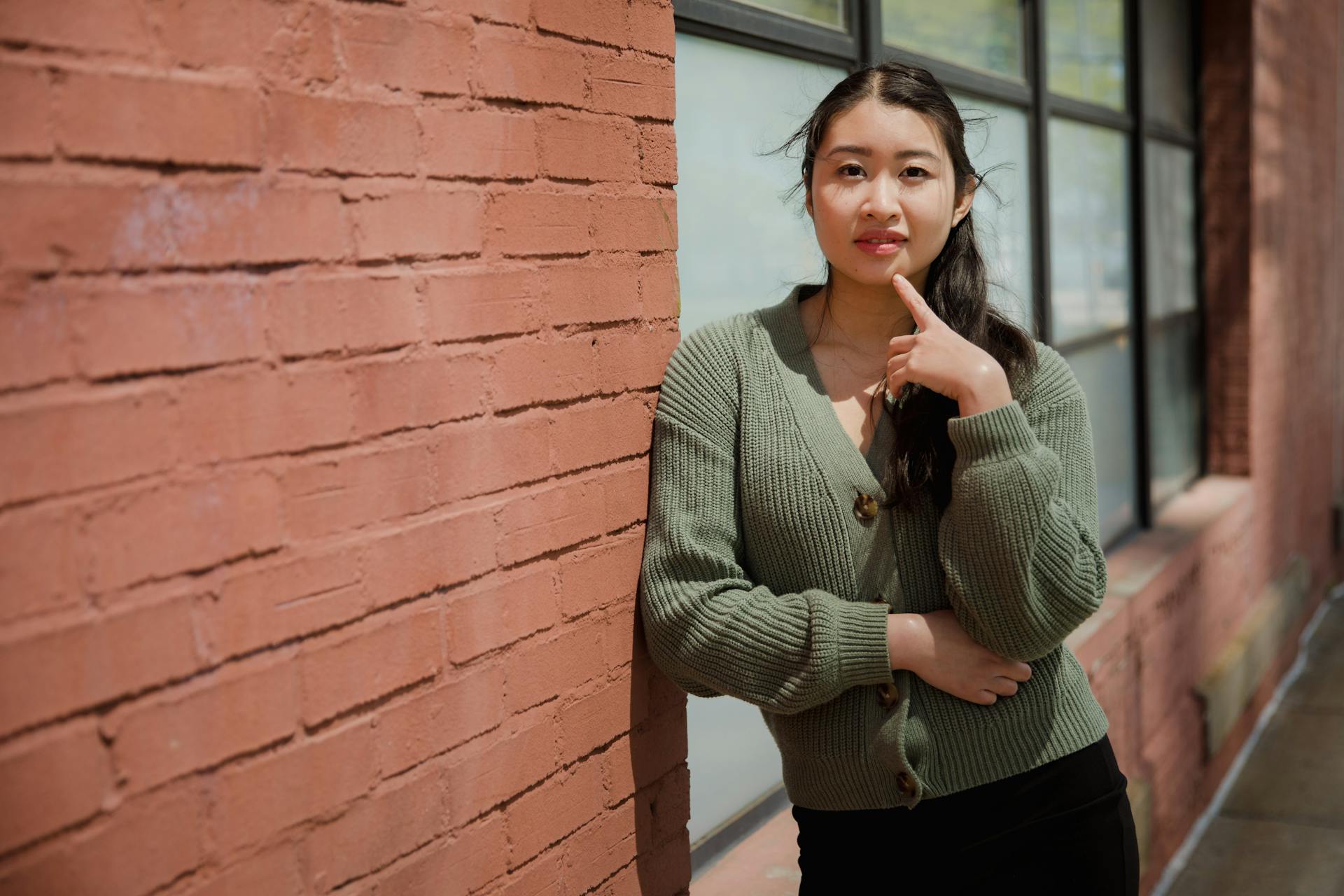 Woman in Knit Cardigan Leaning on Brick Wall