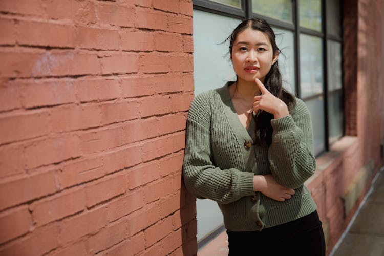 Woman In Knit Cardigan Leaning On Brick Wall