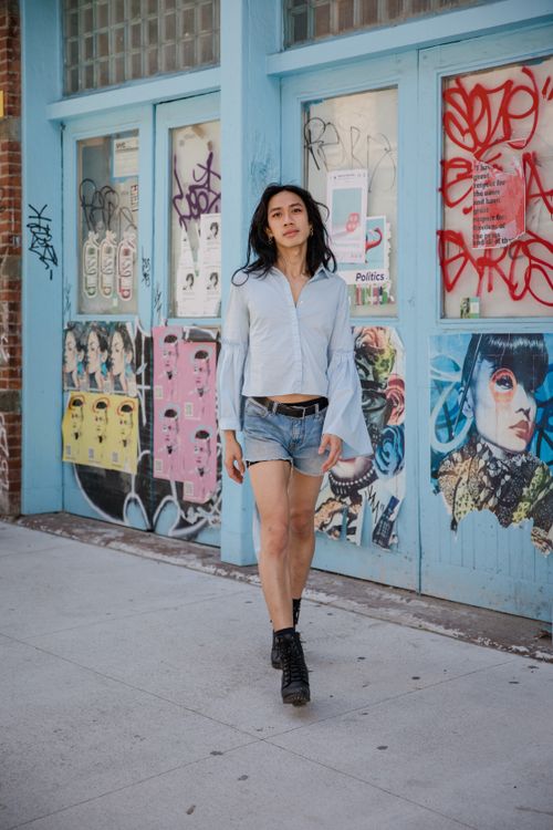Free Asian woman in denim shorts walking by colorful graffiti wall on a sunny day. Stock Photo