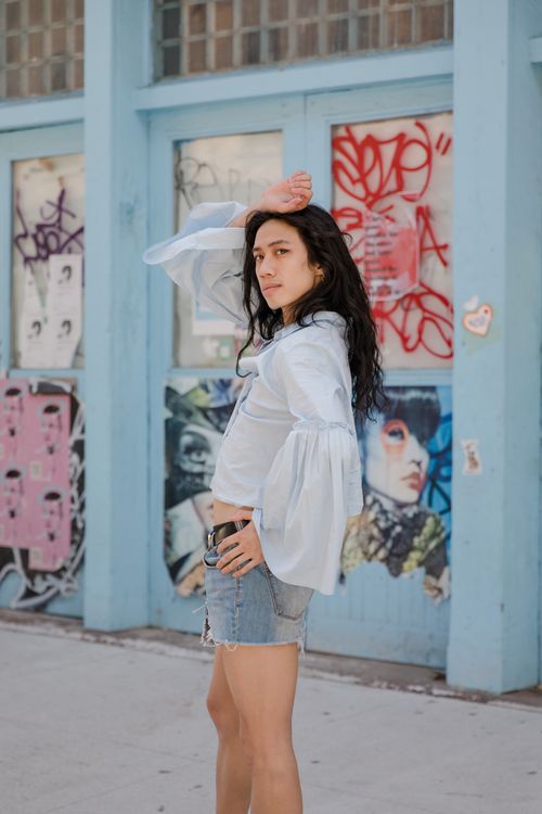 Free Fashionable woman in denim shorts posing confidently on a city sidewalk with vibrant graffiti backdrop. Stock Photo