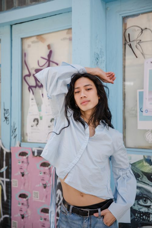 Free Stylish Asian woman posing in denim shorts and white long sleeves on a graffiti-strewn street. Stock Photo