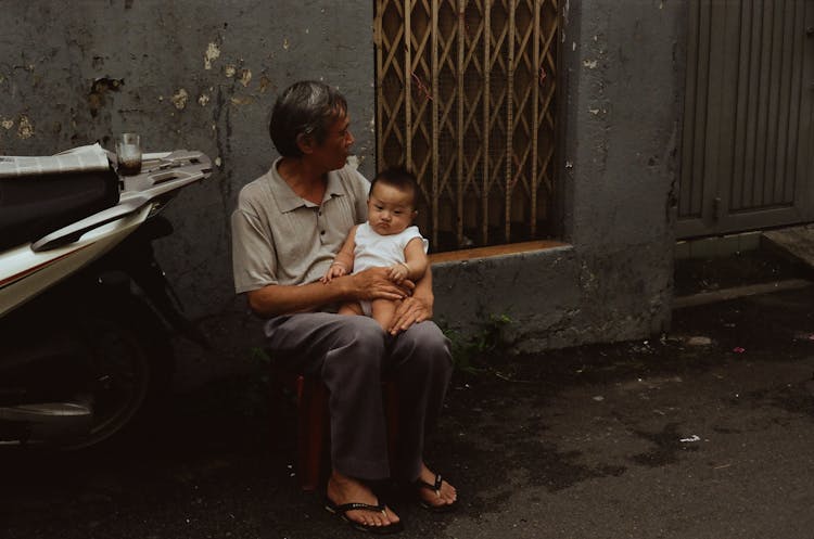 An Elderly Man Sitting While Carrying A Baby