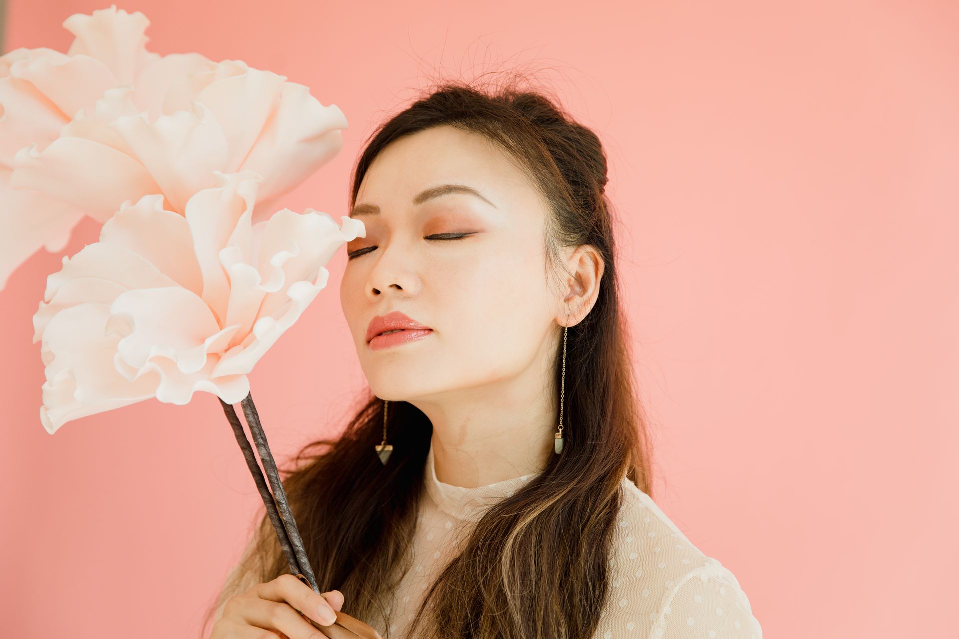 Profile of a serene woman with eyes closed holding delicate flowers, set against a soft pink background.