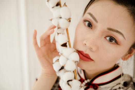 Close-up portrait of a woman with red lips holding a cotton branch gracefully.