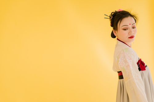 Free Elegant portrait of a woman in traditional Asian dress against a vibrant yellow background. Stock Photo