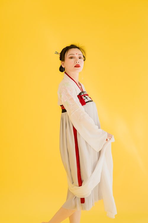 Free Portrait of an Asian woman wearing traditional hanfu, posed elegantly against a bright yellow backdrop. Stock Photo