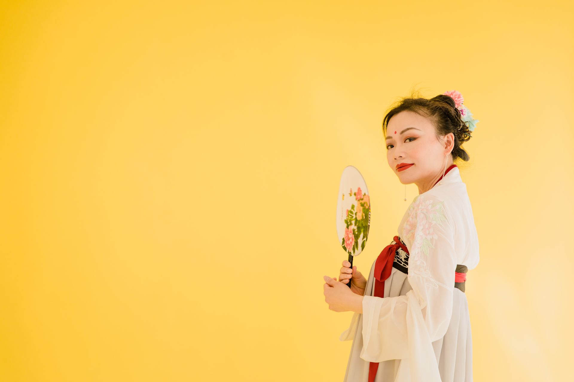 Elegant Asian woman in traditional Hanfu holding a floral fan against a vibrant yellow background.