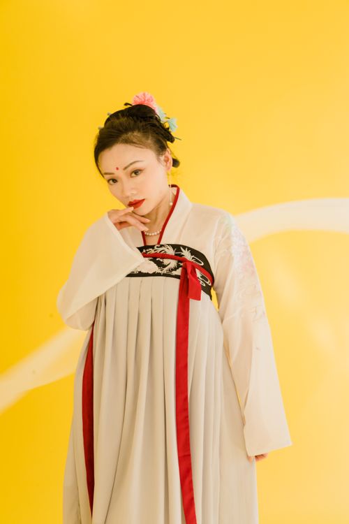 Free A beautiful Asian woman poses gracefully in a traditional Hanfu against a vibrant yellow background. Stock Photo