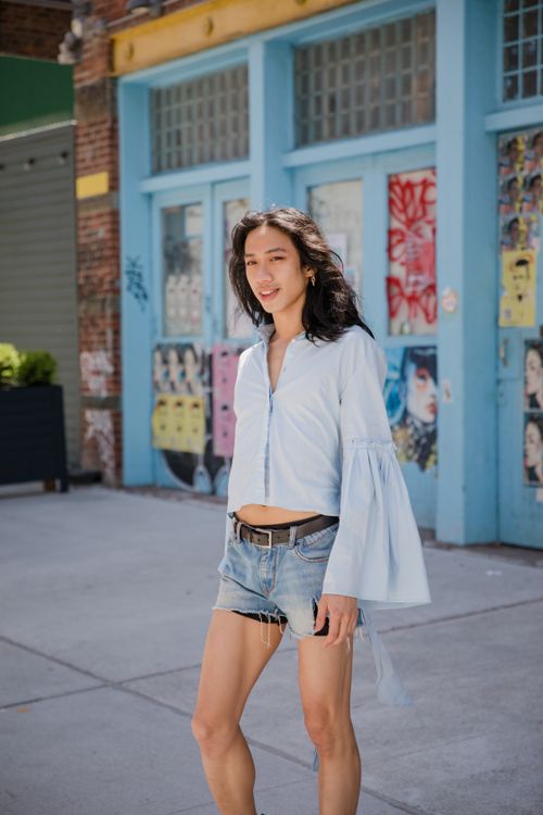 Free Stylish young woman in denim shorts and white top smiling outdoors on sidewalk. Stock Photo