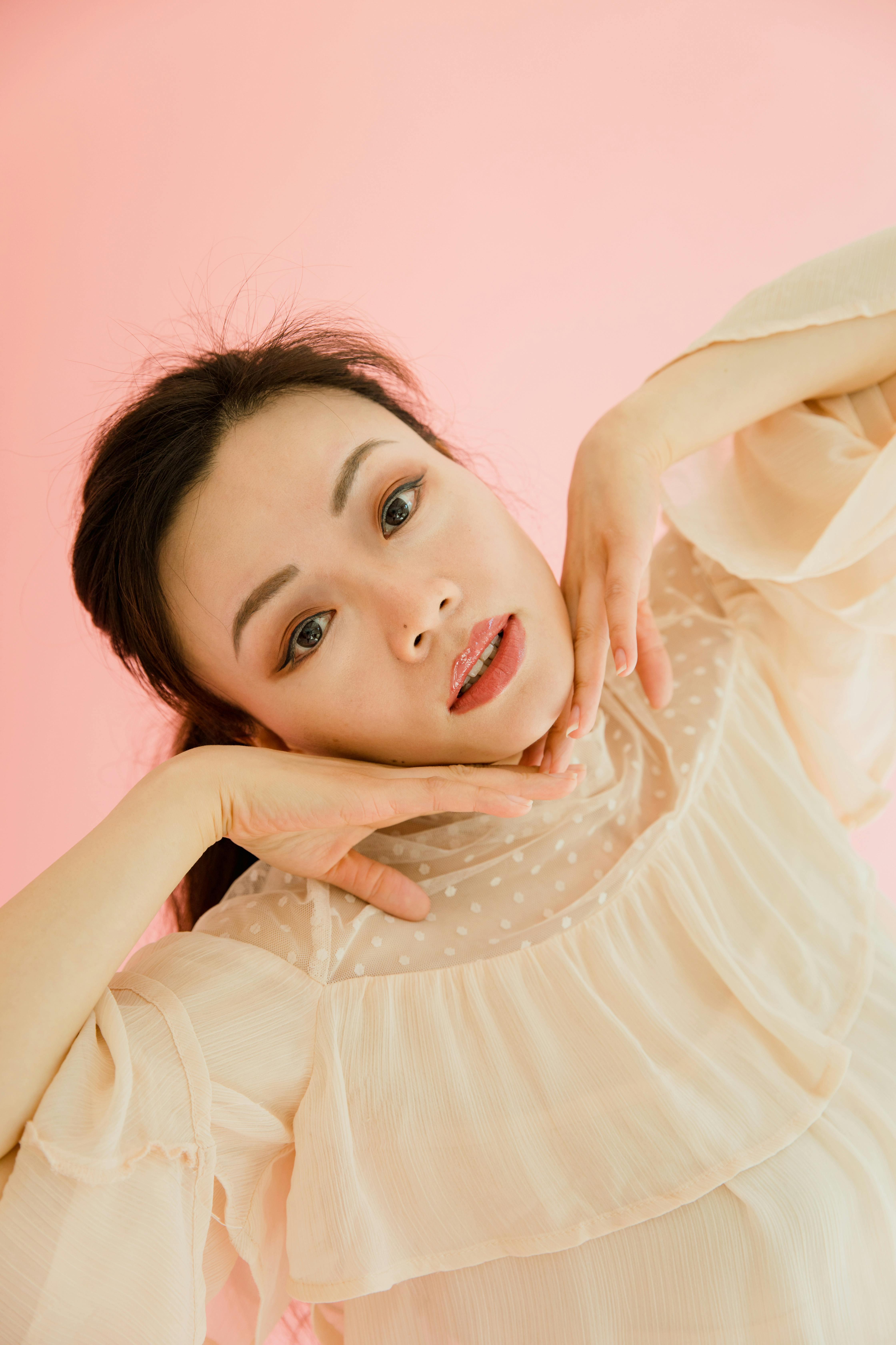 Model in a pink dress posing artistically with a soft pink background in a studio setting.