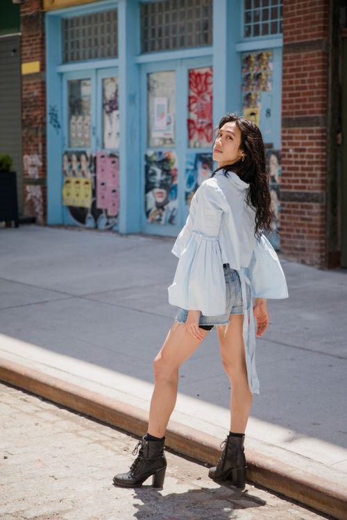 Free Stylish woman in a light blue blouse posing outdoors on a vibrant city street. Stock Photo
