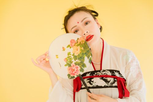Free Asian woman in hanfu holding a floral fan, set against a vibrant yellow background. Stock Photo