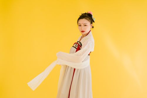 Free Asian woman in traditional attire posing against a vibrant yellow backdrop, exuding elegance and cultural heritage. Stock Photo
