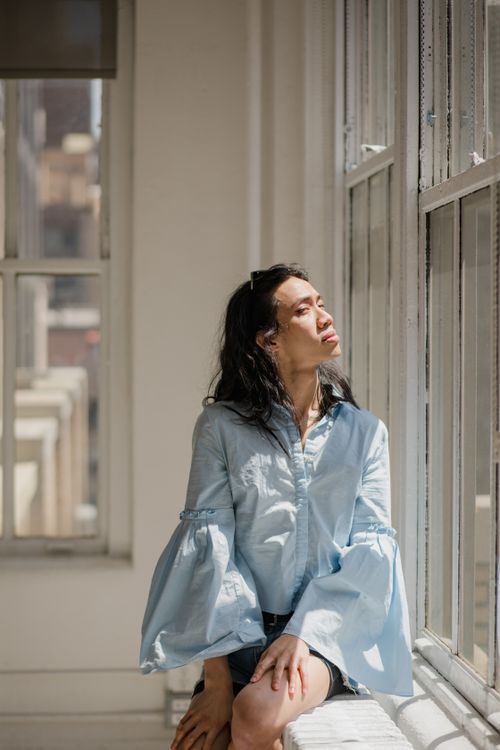 Free Fashionable model in blue long sleeves sits by a bright window indoors. Stock Photo